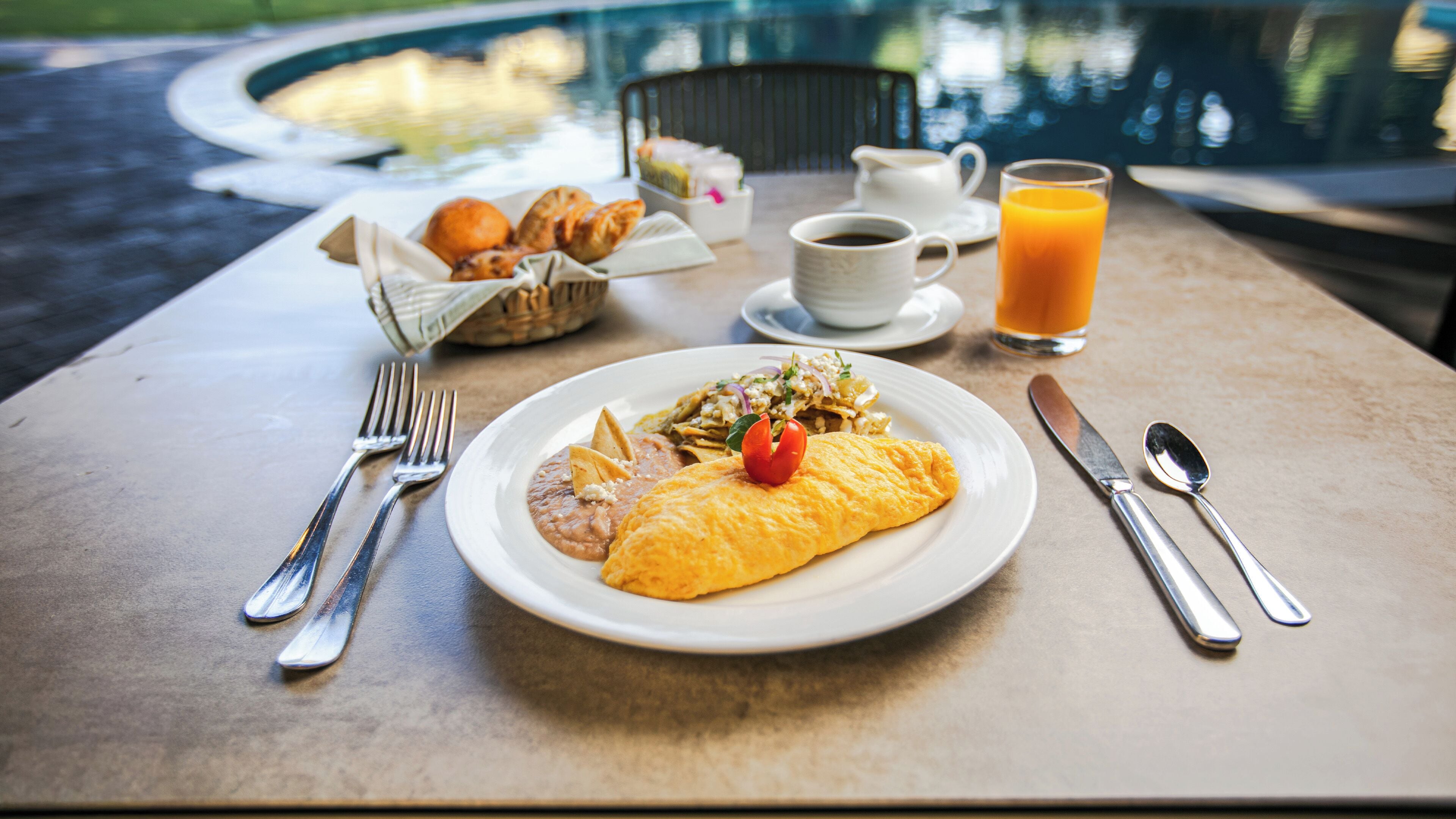 Une table de petit-déjeuner avec une assiette de nourriture, un verre de jus d’orange et une tasse de café.