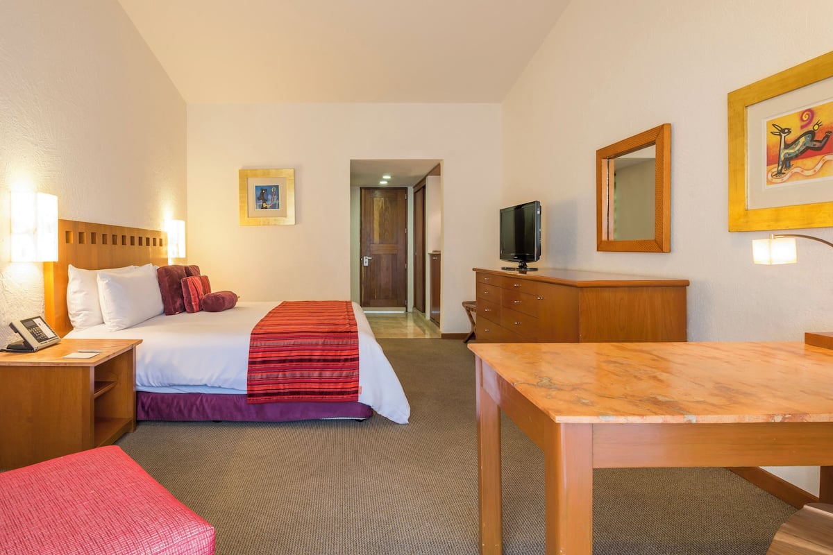 A hotel room with a bed, bedside tables, a desk, a chair, a television, and a mirror.