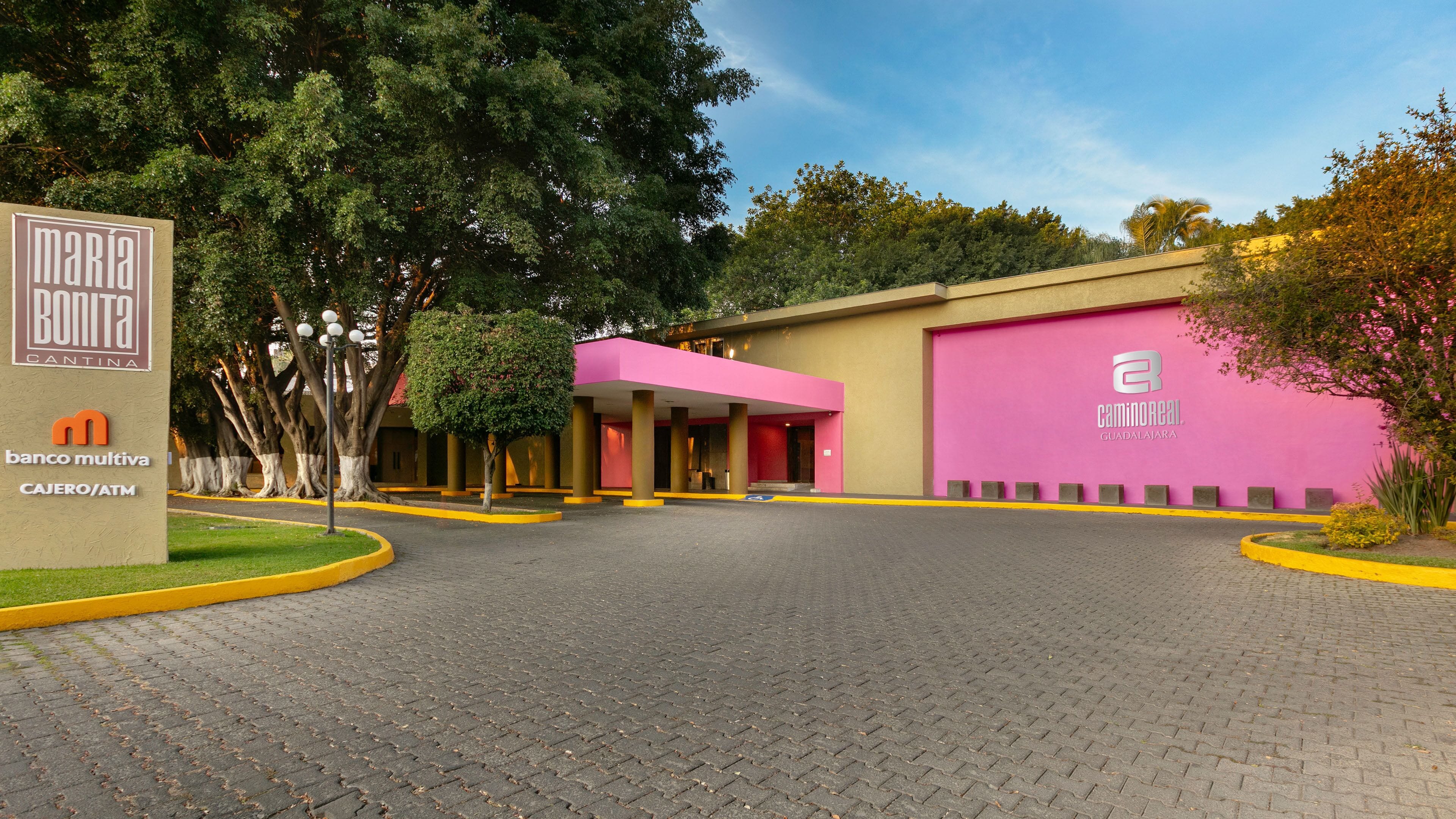 Een gebouw met een roze gevel, een bord met de tekst 'Maria Bonita Cantina' en een geldautomaat van 'Banco Multiva'.