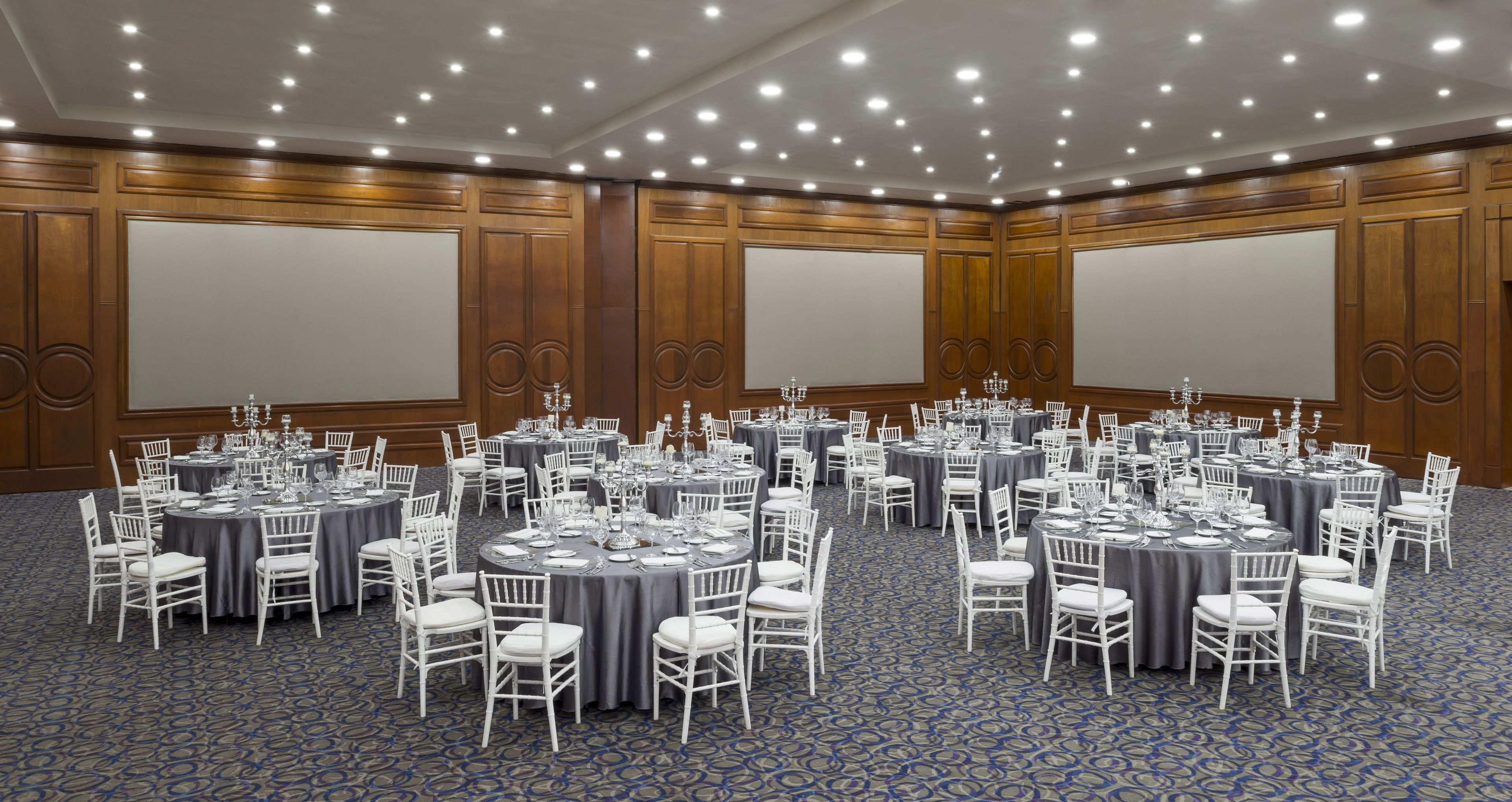 A large conference room with multiple round tables, each set with white chairs and tablecloths, and a blue patterned carpet.