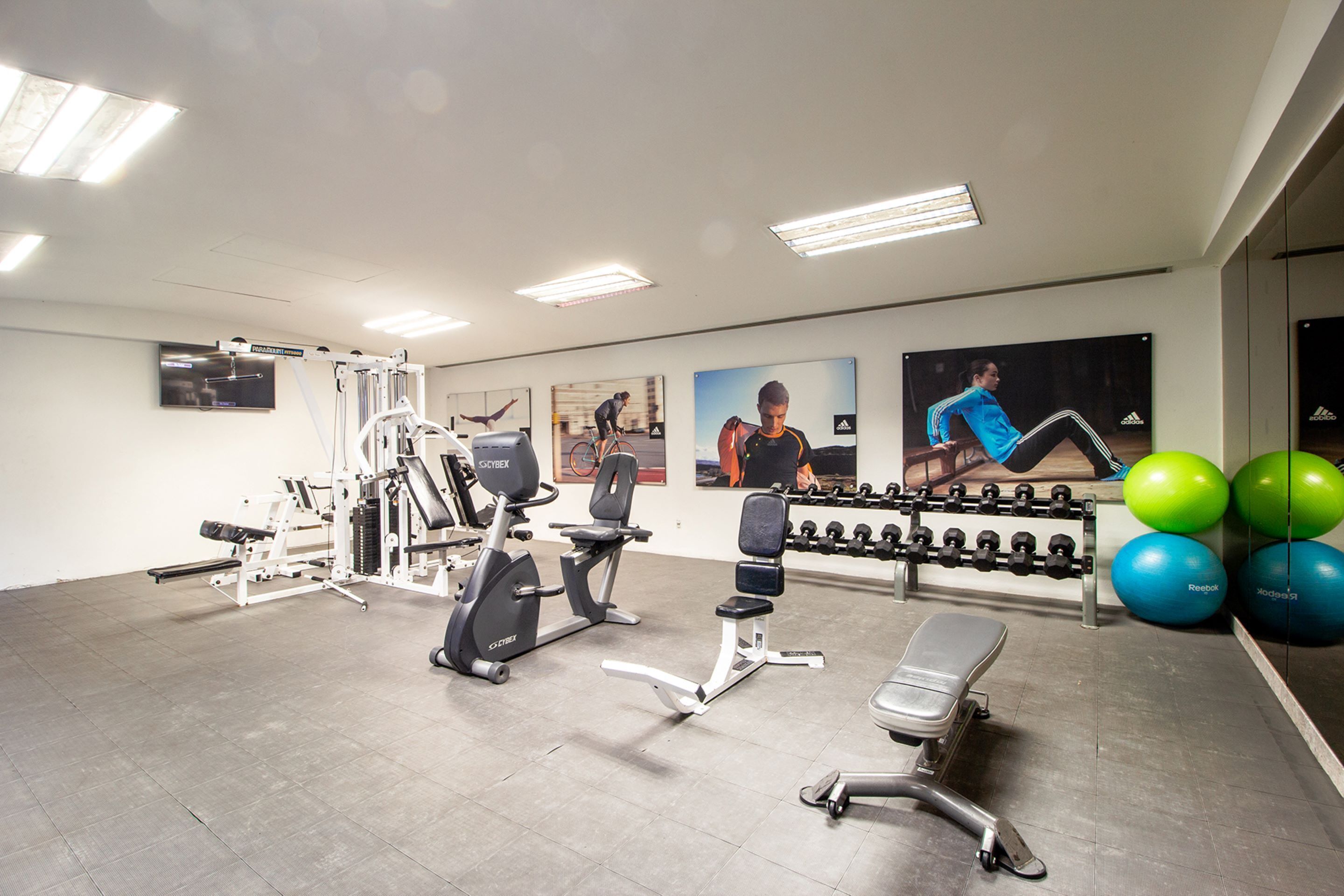 A gym with exercise equipment, a bench, and a wall with posters.