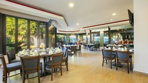 Ein geräumiges Restaurant mit mehreren Tischen und Stühlen, großen Fenstern mit Blick ins Freie und einem klaren, modernen Interieur.