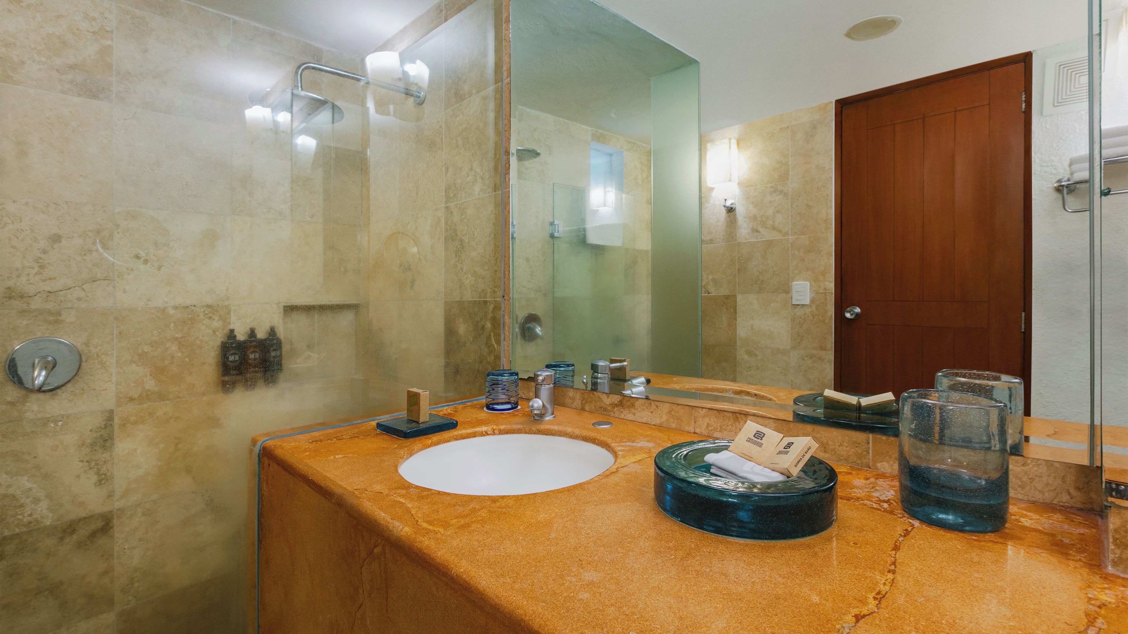 A bathroom with a marble sink, a glass shower enclosure, and a wooden door.