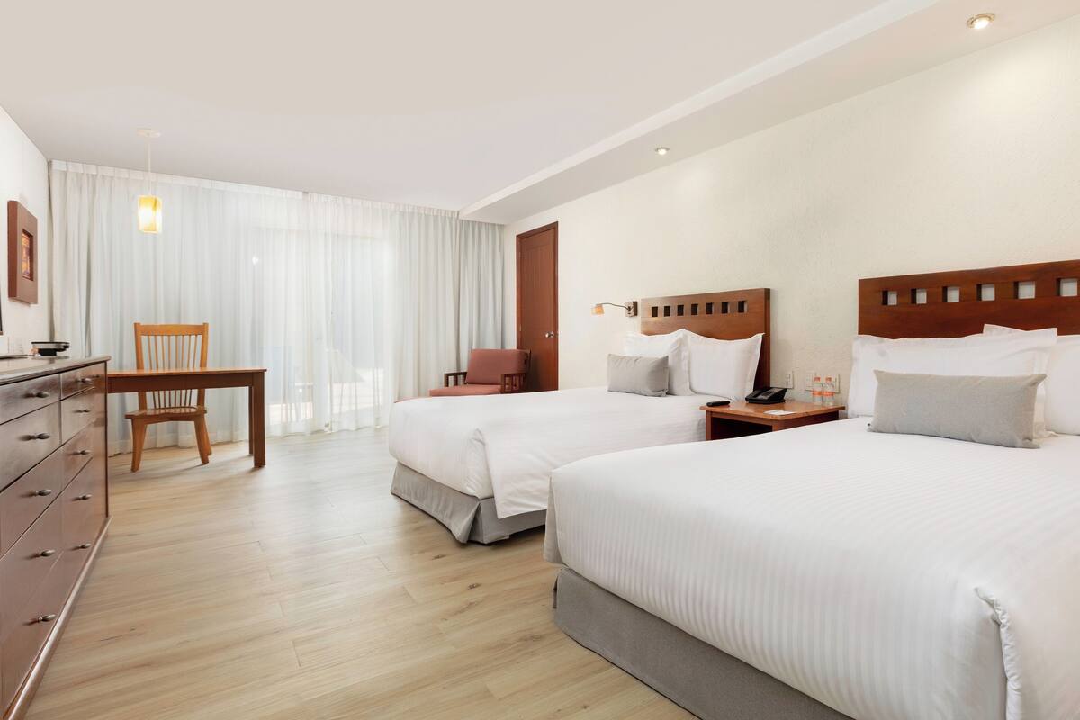 Ein Hotelzimmer mit zwei Betten, einem Schreibtisch, einem Stuhl und einem Essbereich mit Tisch und Stühlen.