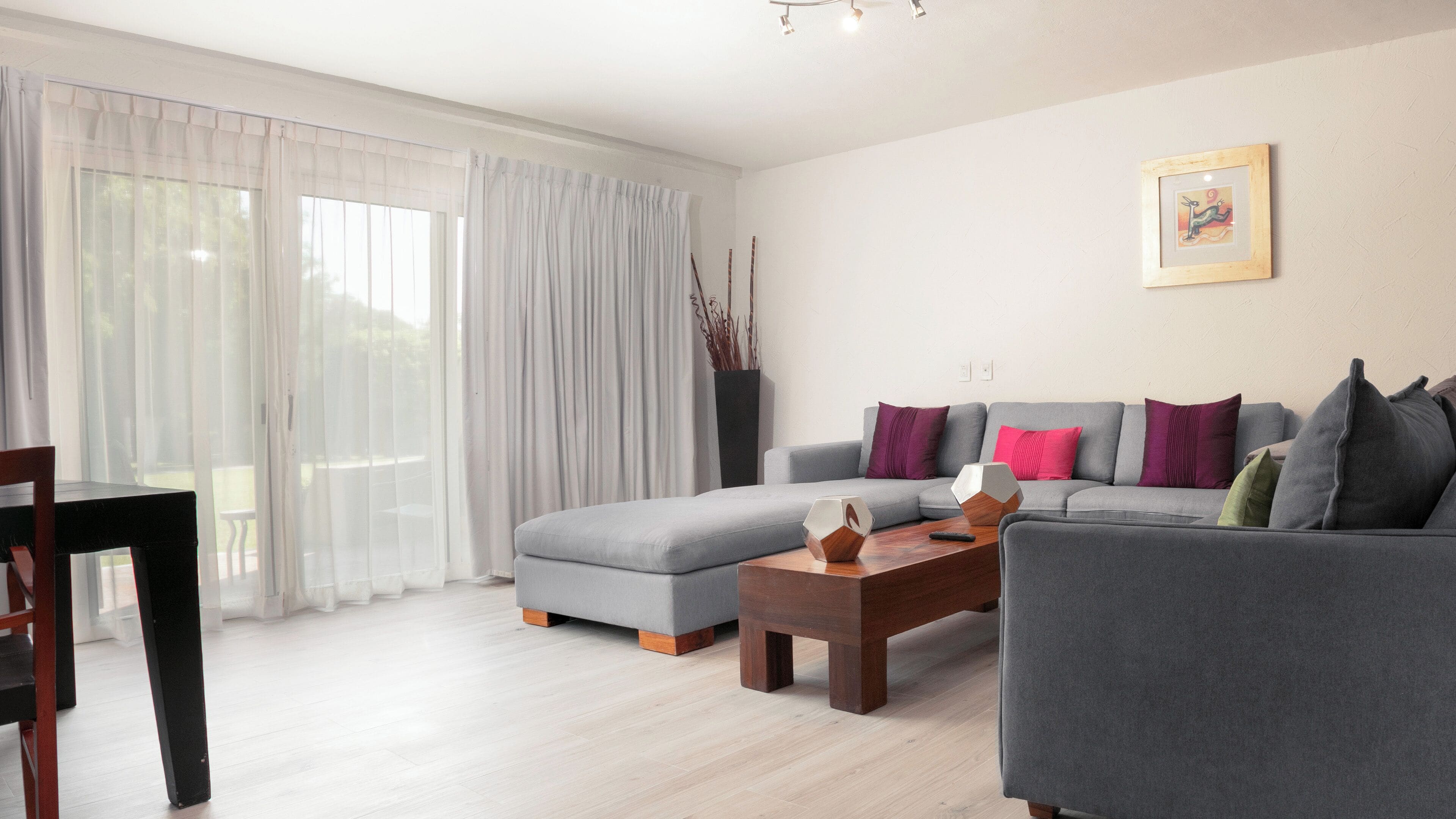 A modern living room with a grey sofa, a wooden coffee table, and a dining area with a table and chairs.