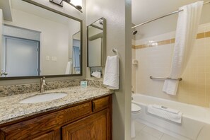 A bathroom with a granite countertop sink, wooden vanity, a large mirror, a towel rack, and a bathtub.