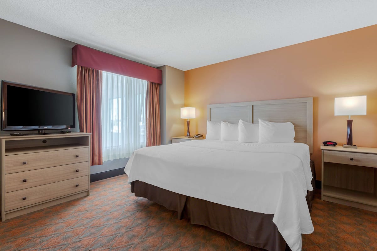 A hotel room with a large bed, a TV on a dresser, and a desk with a lamp.
