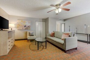A living room with a sofa, armchair, coffee table, TV, and ceiling fan.
