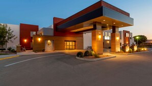 Un hotel moderno con un'ampia hall, una zona esterna coperta e una facciata ben illuminata.