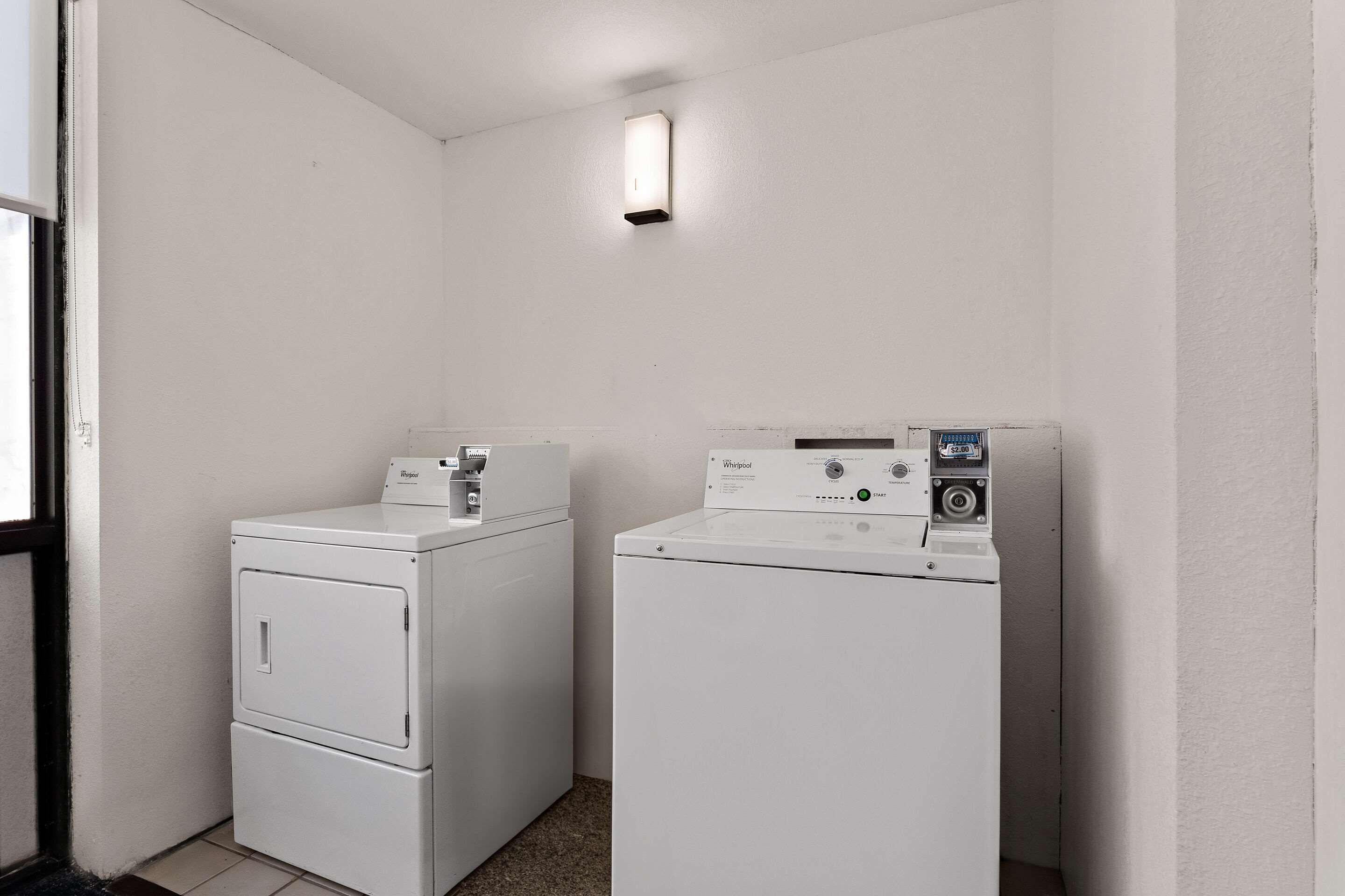 A laundry room with two stacked washers and a dryer, a light fixture above the dryers, and a door to the left.