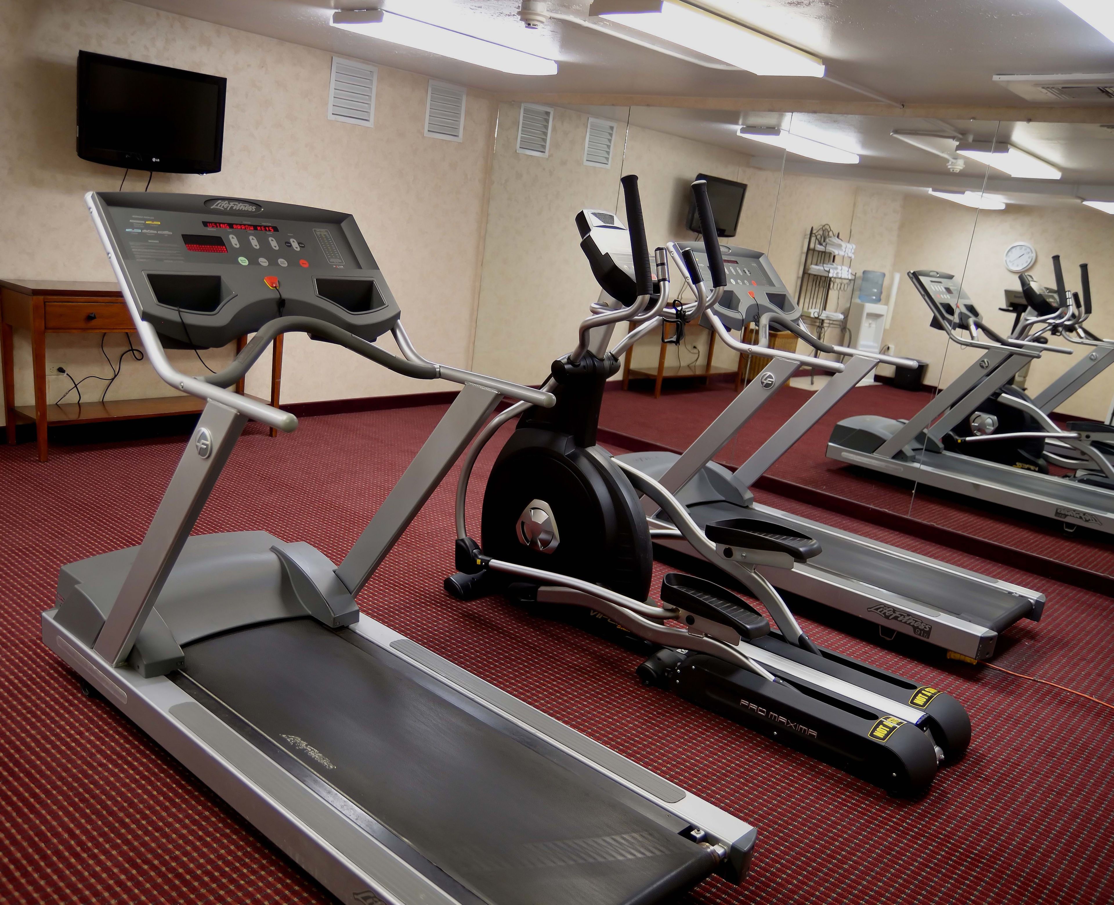 A gym with treadmills, exercise bikes, and a TV on the wall.