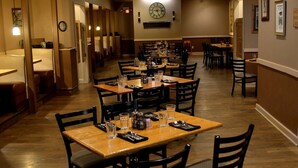 A restaurant with multiple tables and chairs, wooden flooring, and a clock on the wall.
