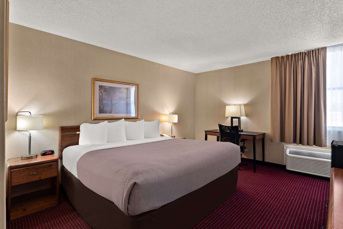 A hotel room with a large bed, bedside tables with lamps, a desk with a chair, and a window with curtains.