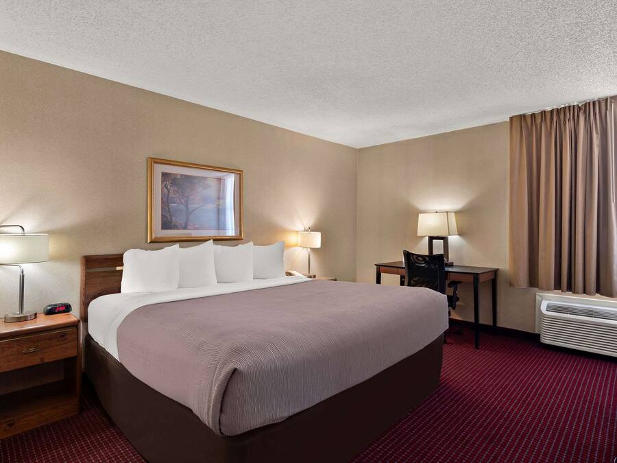 A hotel room with a large bed, bedside tables with lamps, a desk with a chair, and a window with curtains.