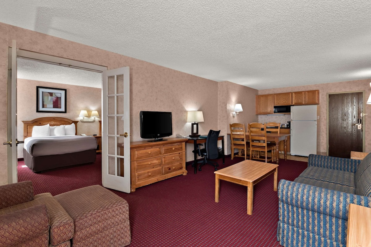 A hotel room with a bed, a desk, a television, a kitchenette, and a seating area.