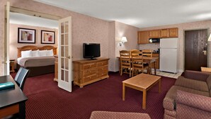 A hotel room with a bed, a TV, a dining table with chairs, a kitchen area with a microwave and refrigerator, and a sofa.
