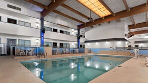 An indoor swimming pool with a clear water surface, surrounded by a tiled floor and a wooden ceiling structure.