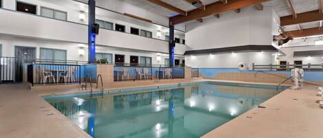 An indoor swimming pool with a clear water surface, surrounded by a tiled floor and a wooden ceiling structure.