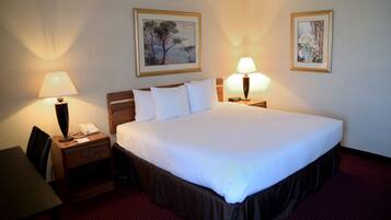 A hotel room with a large bed, two bedside lamps, a desk with a chair, and two framed pictures on the wall.