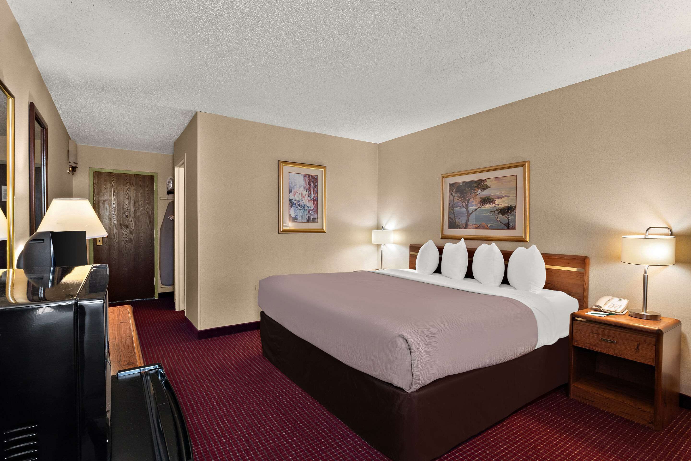 Habitación de hotel con una cama grande, dos mesitas de noche con lámparas, un escritorio con teléfono y un espejo.
