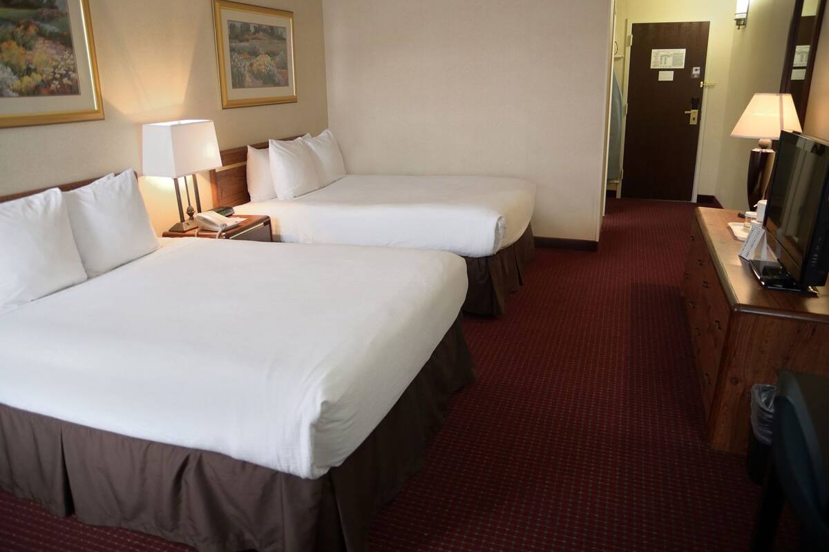 A hotel room with two beds, a desk with a lamp, and a television.