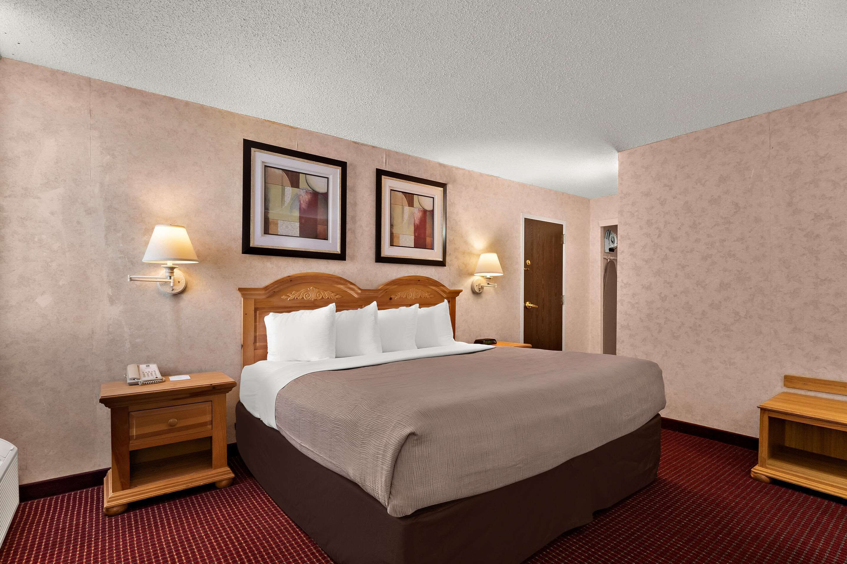Habitación de hotel con una cama grande, dos mesitas de noche con lámparas, un cabecero de madera y dos cuadros enmarcados en la pared.