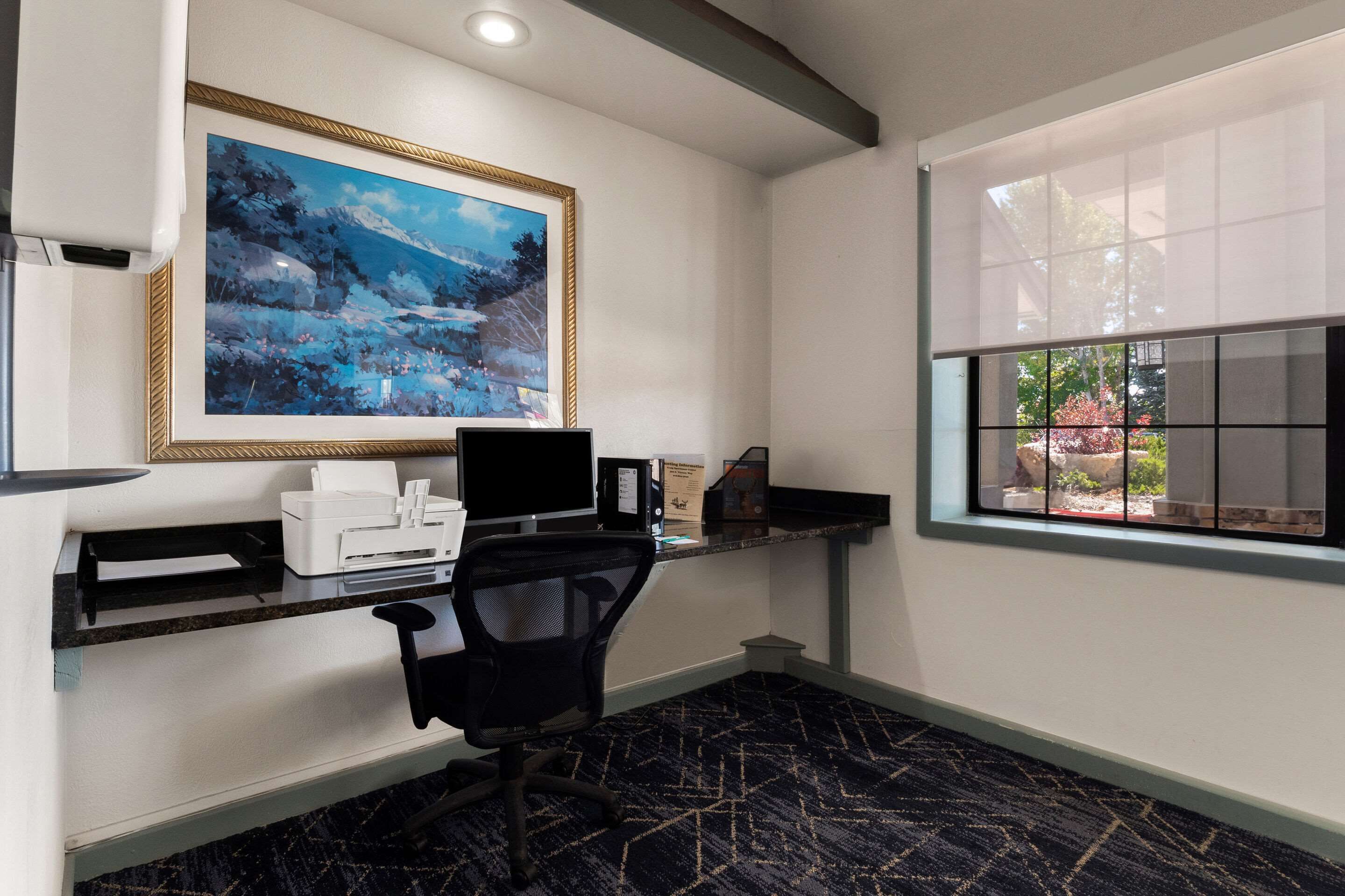 A modern office with a desk, chair, printer, and framed artwork.