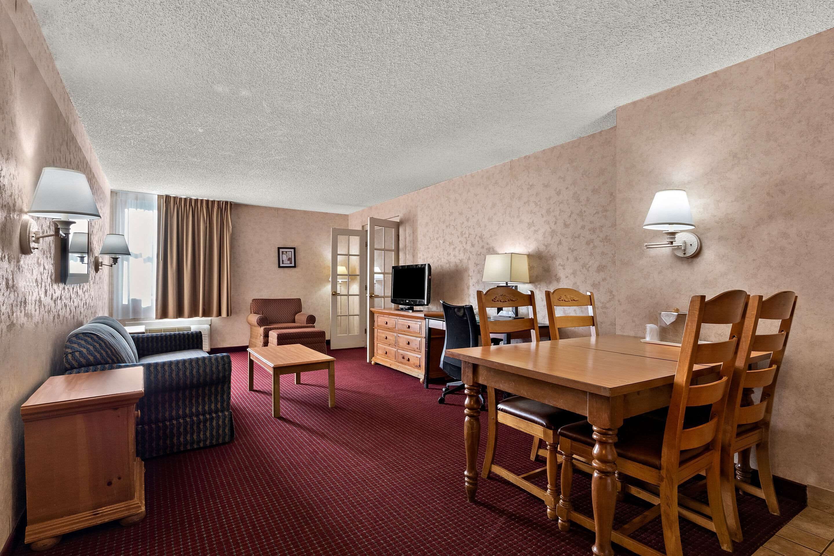 A hotel room with a dining area, a sofa, a TV, and a desk.