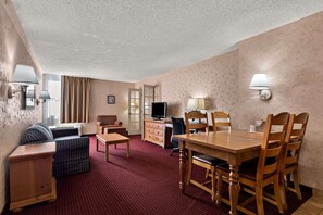 A hotel room with a dining area, a sofa, a TV, and a desk.