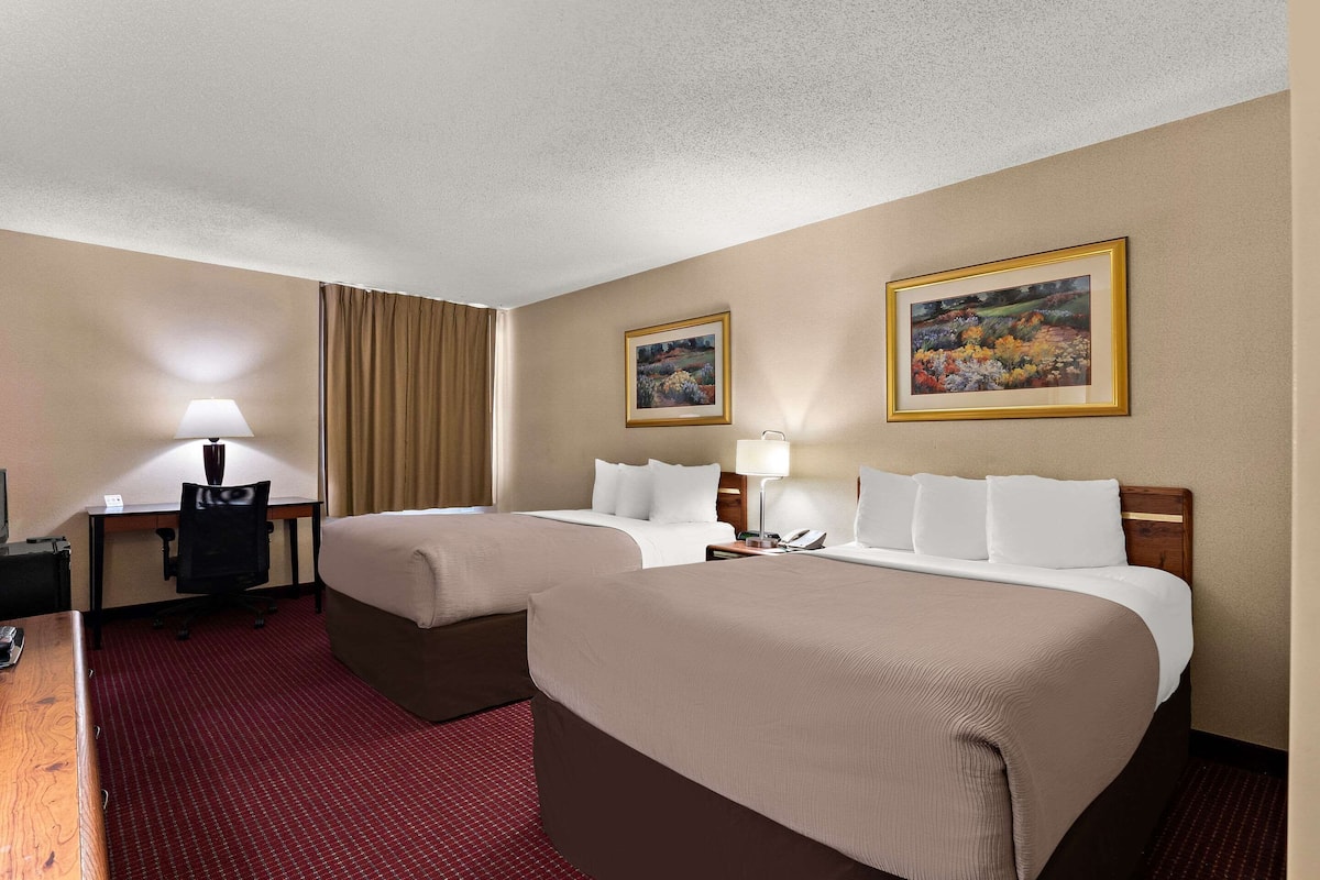 A hotel room with two beds, a desk, a chair, and two paintings on the wall.