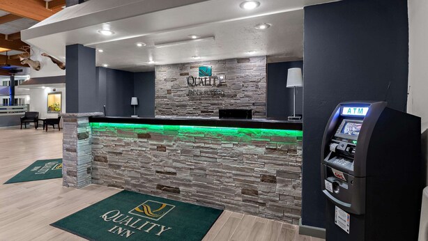 A hotel reception area with a stone counter, an ATM, and a green carpet with the hotel logo.
