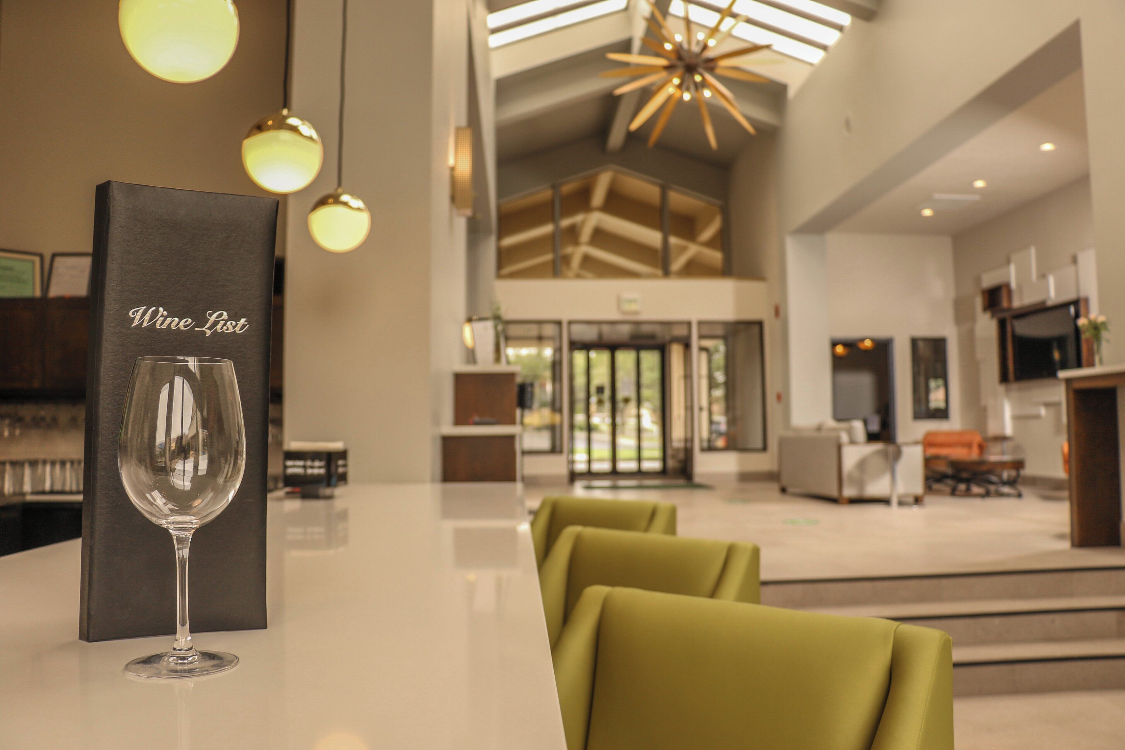 A hotel lobby with a reception desk, a wine list sign, and a glass of wine.