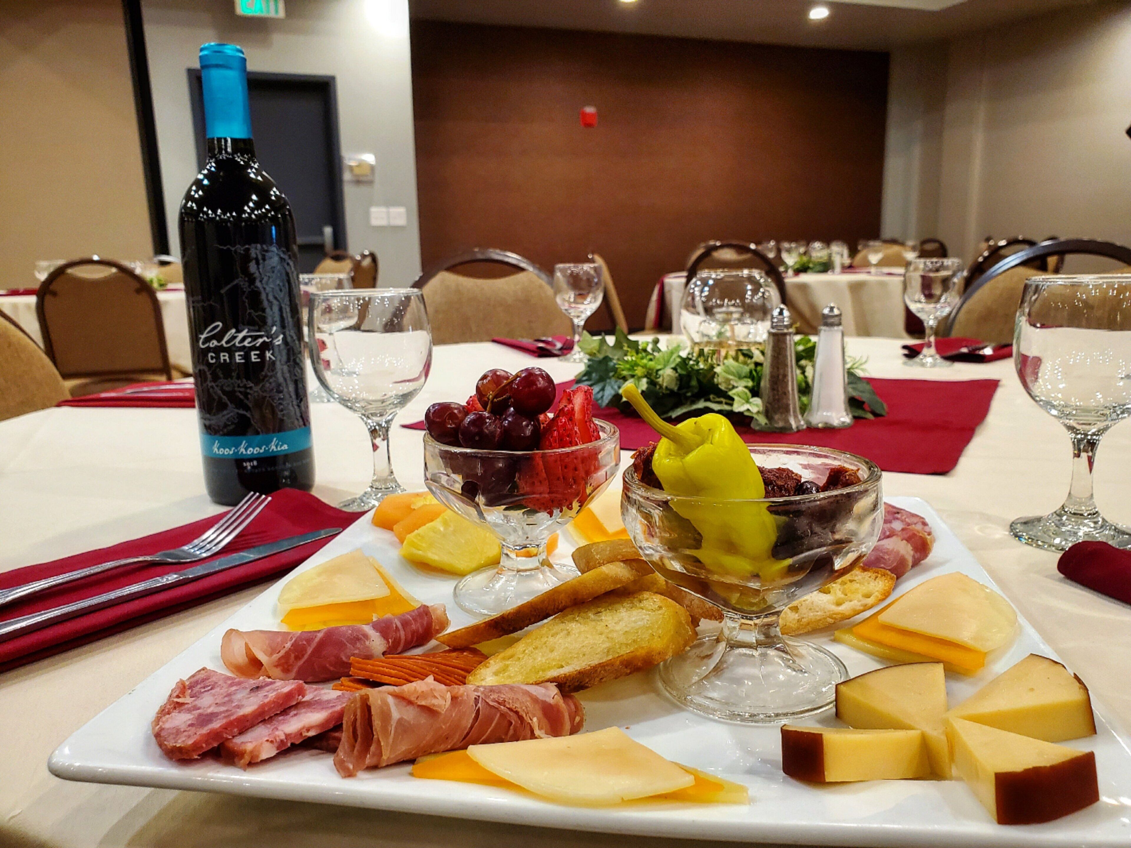 Una mesa de comedor con una variedad de quesos, embutidos y frutas, acompañada de copas de vino y una botella.