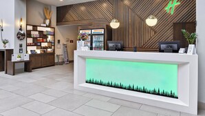 A reception desk with a green-lit display, wooden paneling, and a modern light fixture. - Holiday Inn Clarkston - Lewiston by IHG (Clarkston)