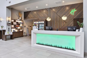 A reception desk with a green-lit display, wooden paneling, and a modern light fixture.