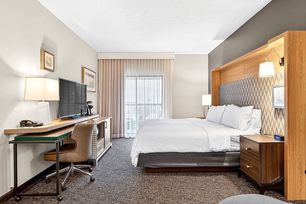 A hotel room with a bed, desk, chair, TV, and a window with curtains.