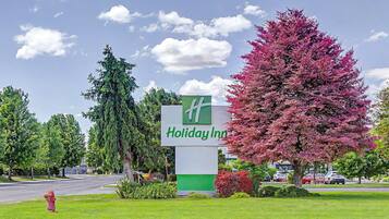 Et Holiday Inn skilt med logo i grøn og hvid, omgivet af frodig vegetation og en klar himmel.
