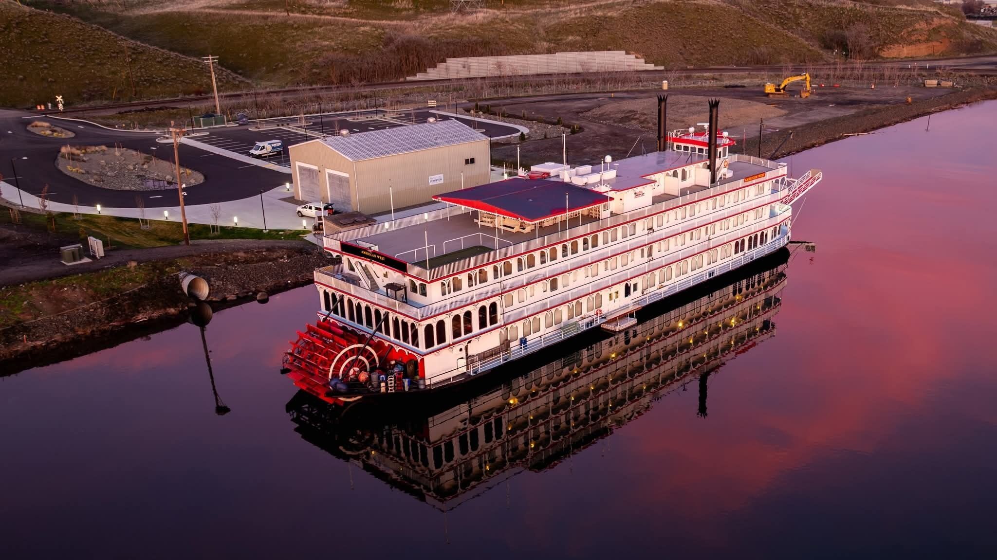 A large riverboat docked at a port with a flat roof and multiple decks.