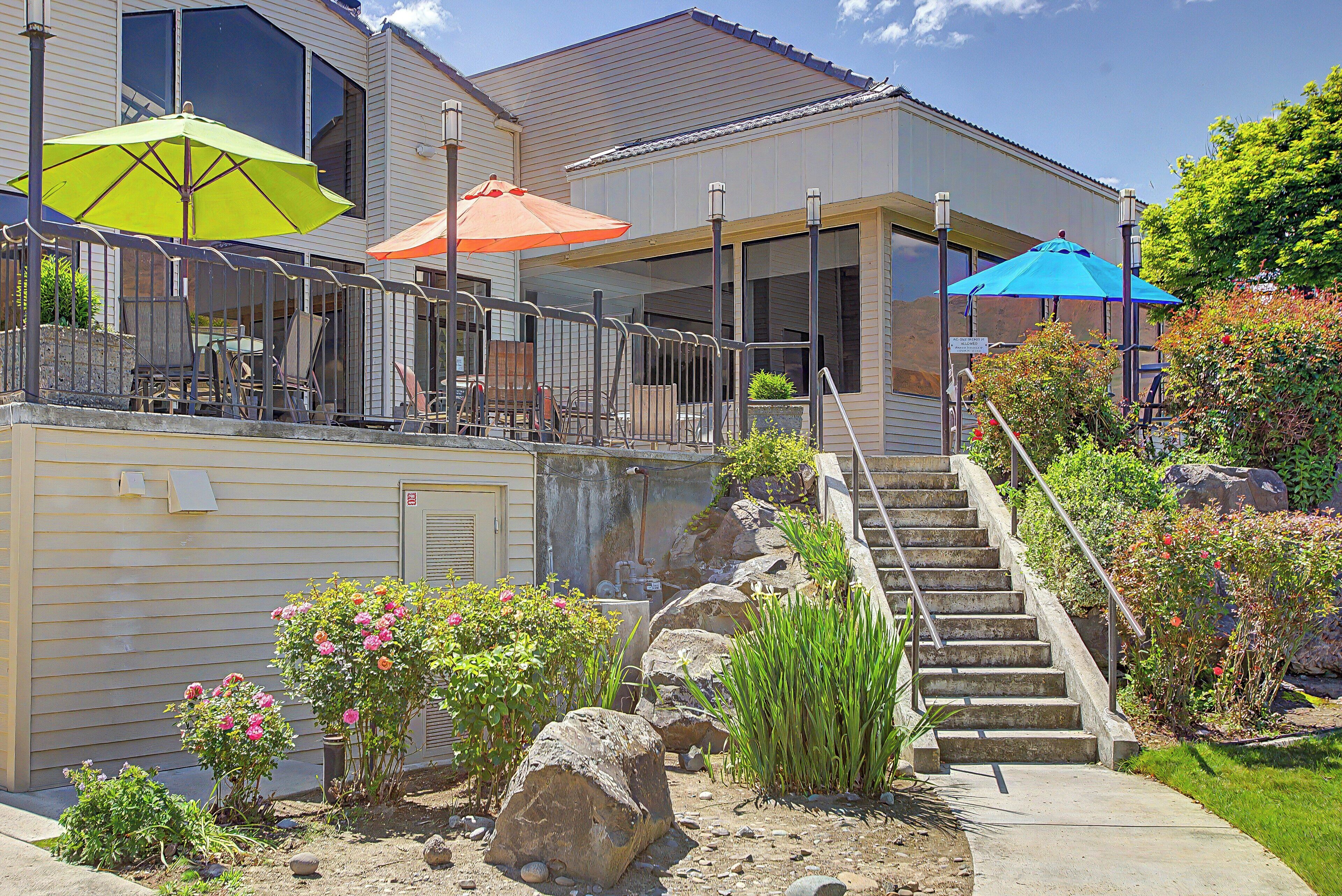 A building with a covered outdoor seating area, a staircase, and a garden with rocks and plants.