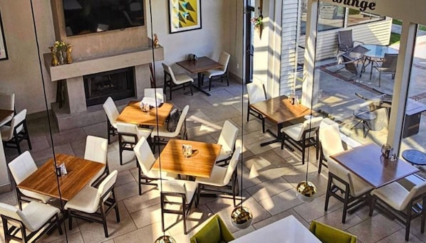A modern indoor dining area with multiple tables and chairs, a fireplace, and a view of the outdoor seating area.