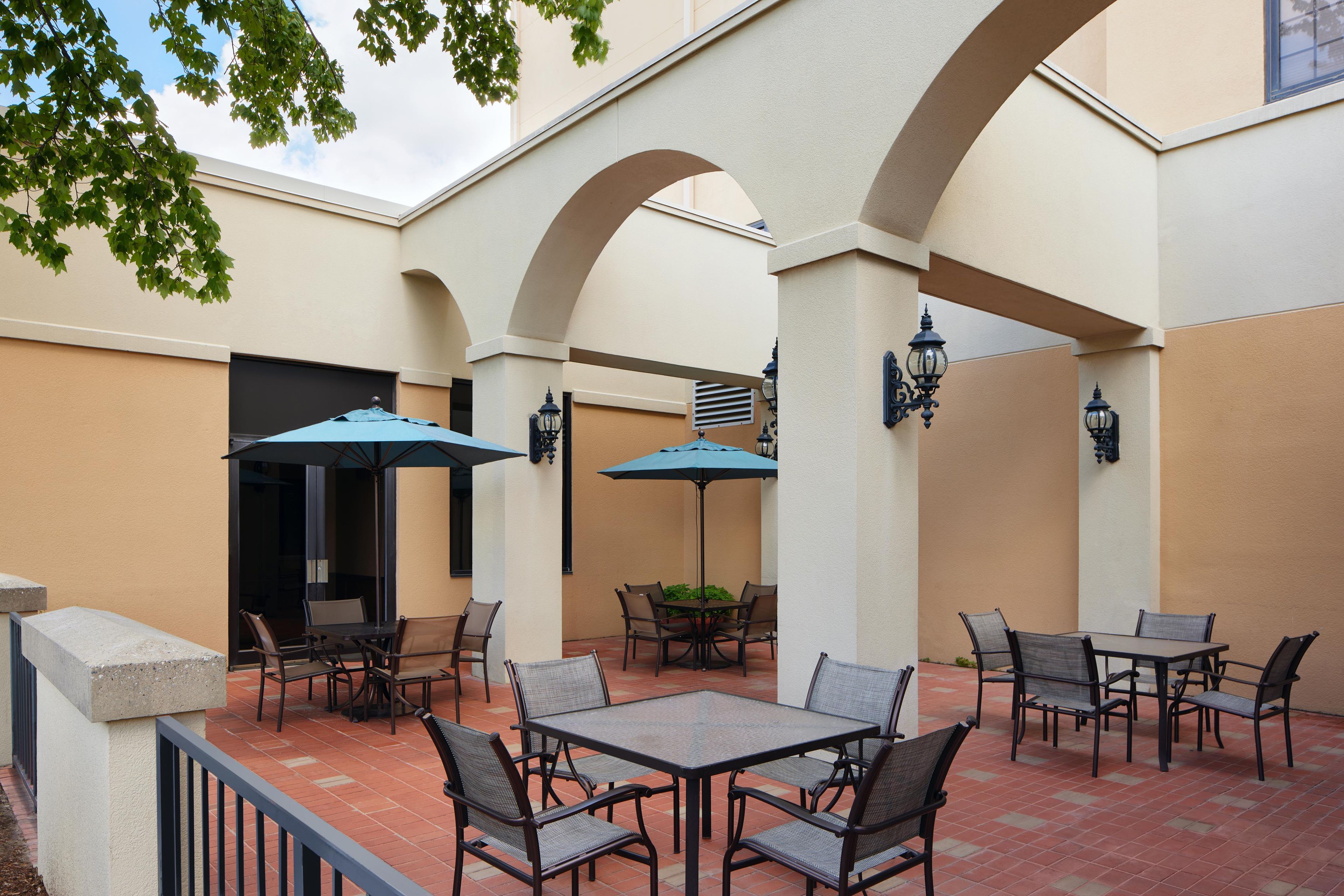 An outdoor patio area with tables and chairs, surrounded by arches and walls.