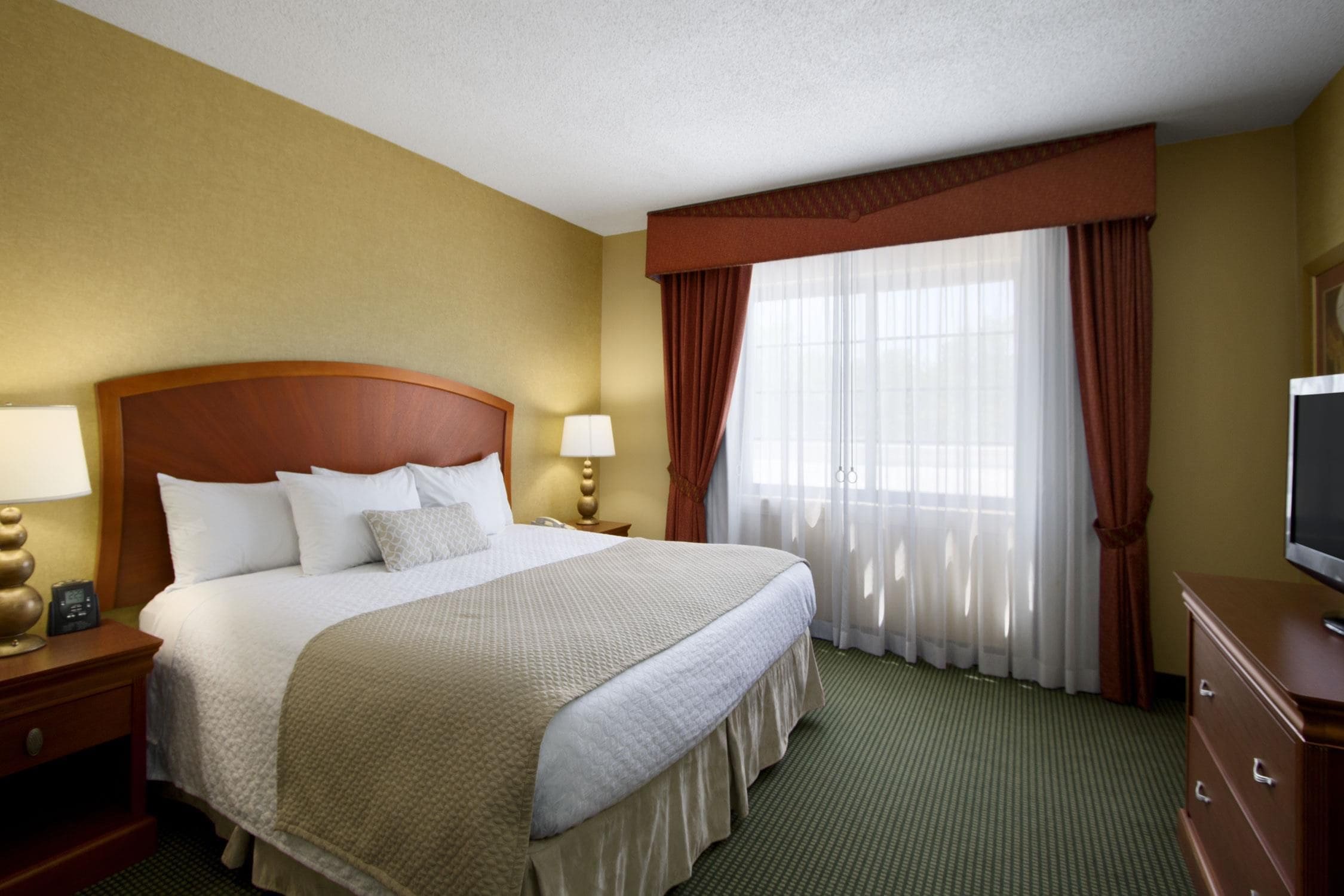 A hotel room with a large bed, two bedside tables with lamps, a television, and a window with curtains.