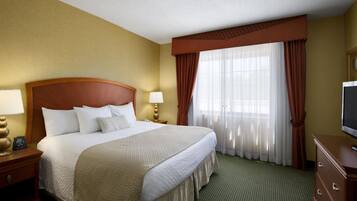 A hotel room with a large bed, two bedside tables with lamps, a television, and a window with curtains.