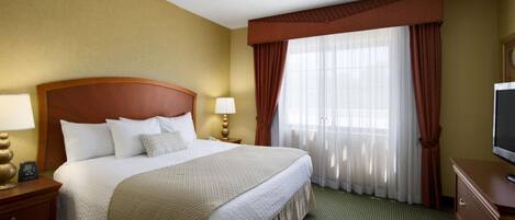 A hotel room with a large bed, two bedside tables with lamps, a television, and a window with curtains.
