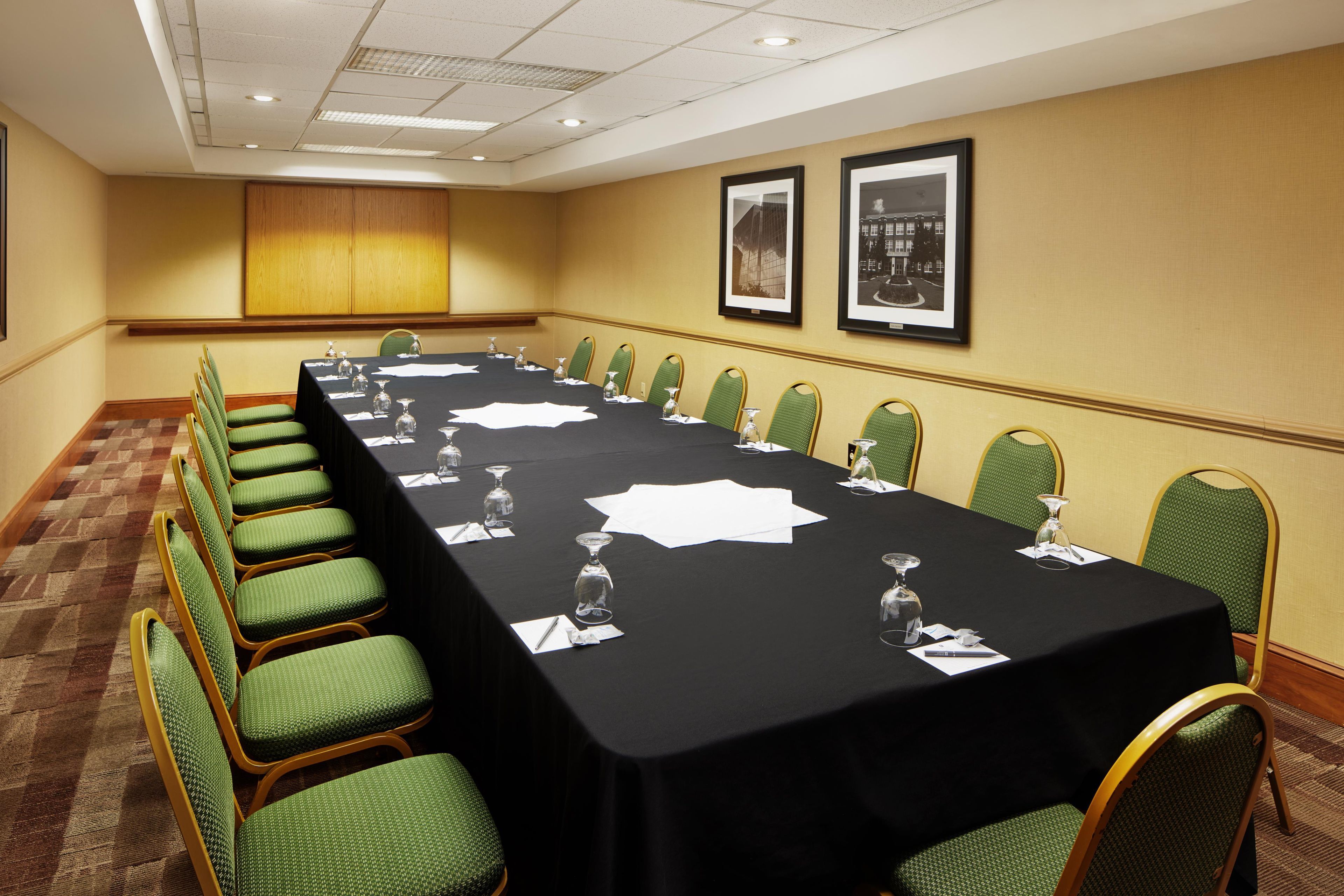 A conference room with a long table, green chairs, and framed pictures on the wall.