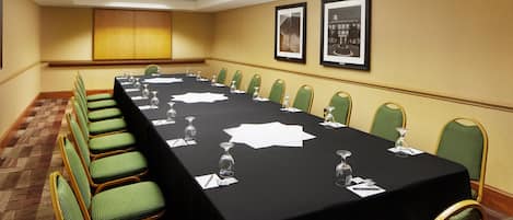 Un salón de conferencias con una larga mesa, sillas verdes y cuadros en la pared.