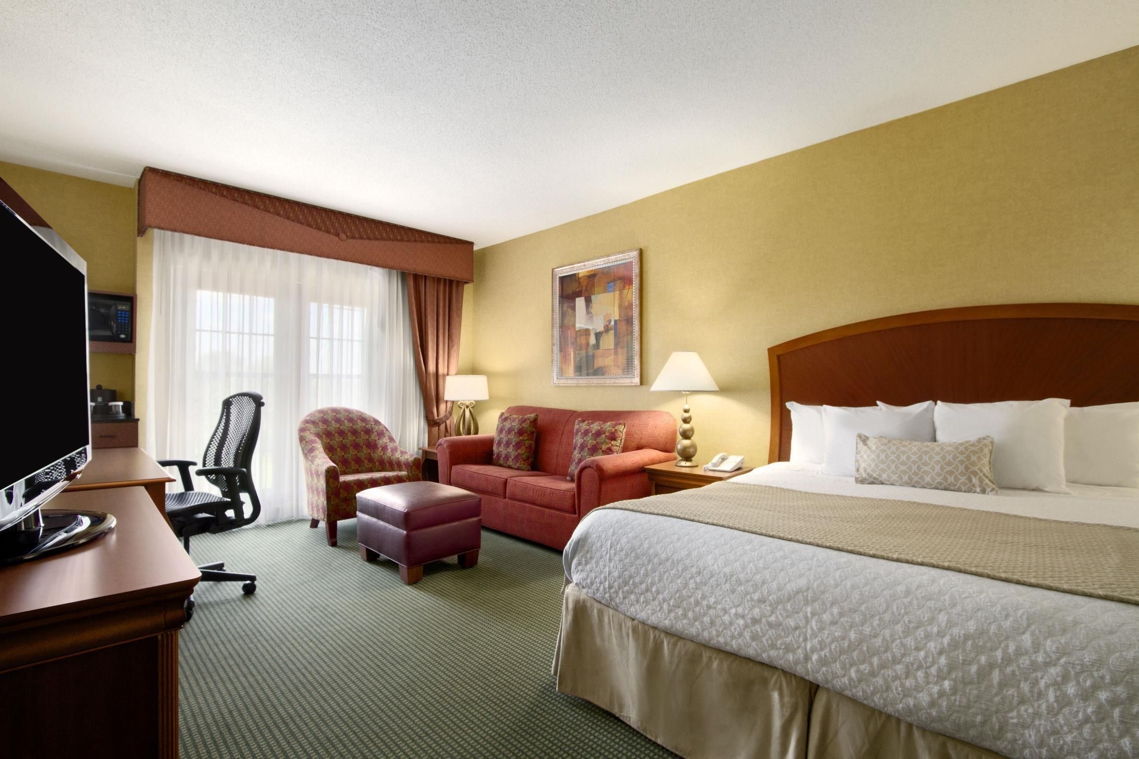 Habitación de hotel con cama, escritorio con televisor, sillón, sofá y un cuadro en la pared.