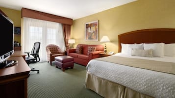 A hotel room with a bed, a desk with a television, a chair, a sofa, and a painting on the wall.