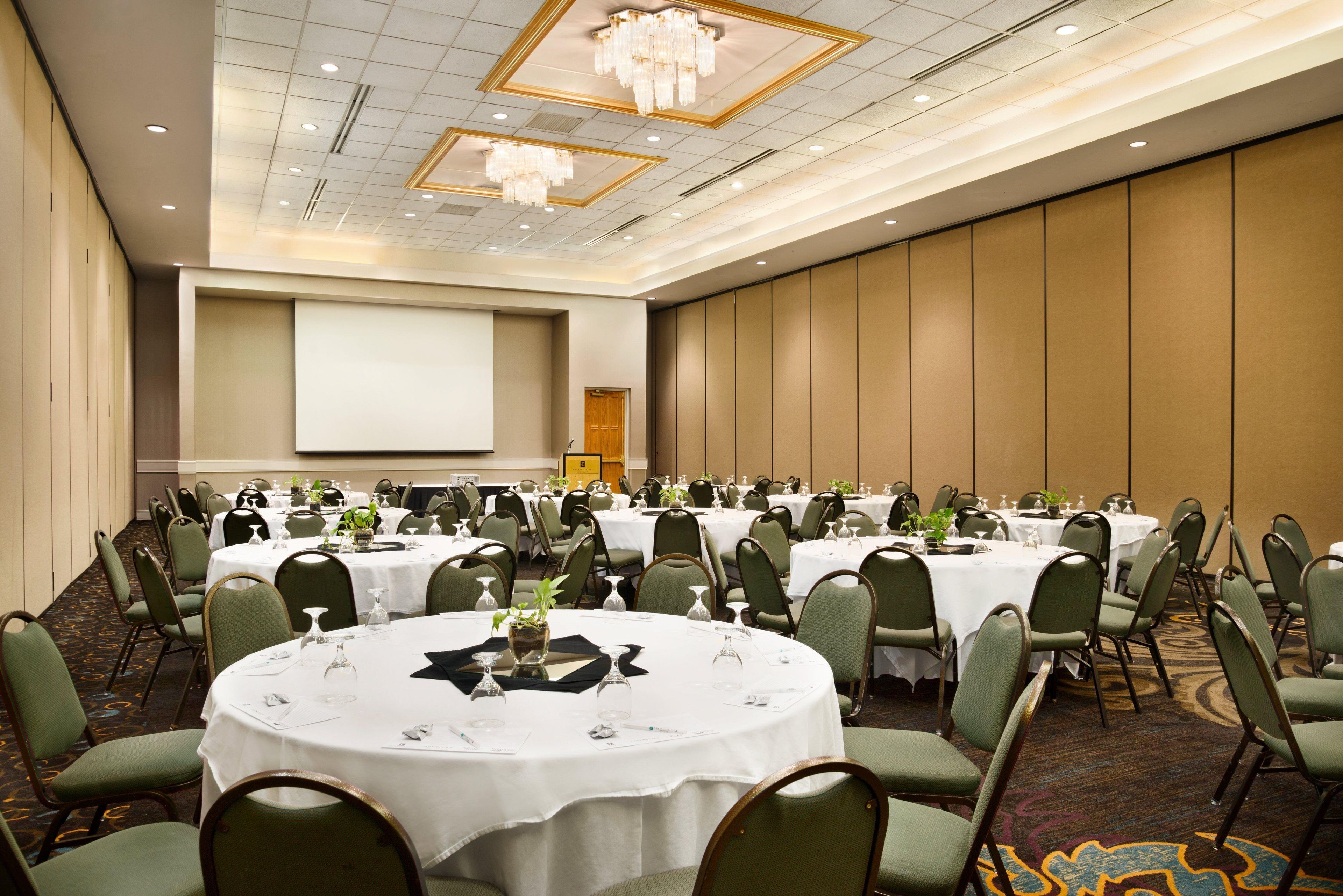 A conference room with multiple tables, chairs, and a large screen.