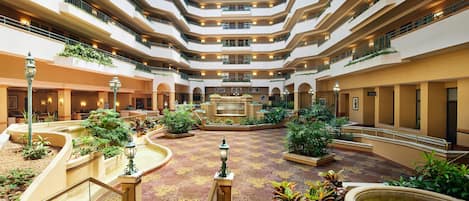 A multi-level atrium with a central fountain, surrounded by greenery and multiple floors with balconies.